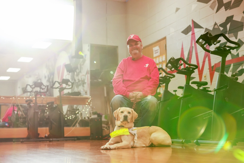 Charles and his guide dog Tango sitting in a gym together